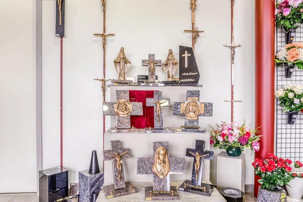 Exposition de croix funéraires en granit et statues religieuses dorées sur présentoir